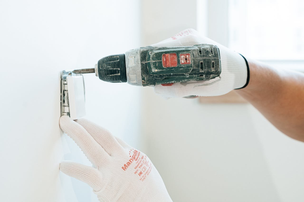gallery-01 Gloved hands using a drill to install a power outlet on a wall, focusing on precision and safety.